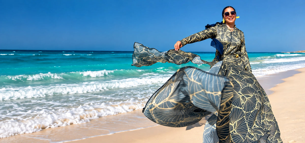 Model wearing Tallah's olive and cream leaf-patterned Burkini with a flowing matching cover-up on a turquoise beach.