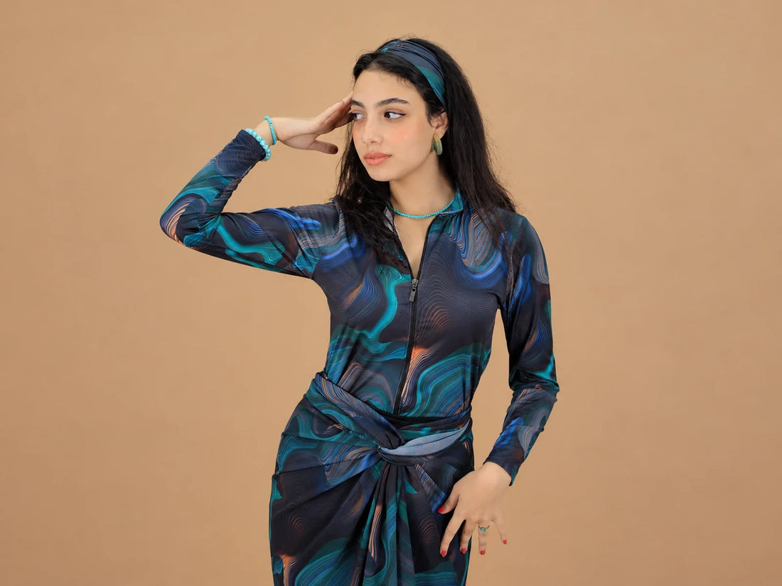 Model wearing a blue and teal patterned long-sleeved Burkini against a warm beige background.