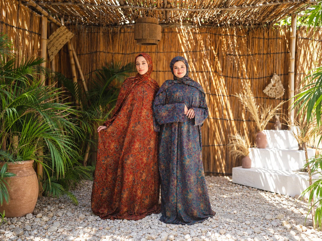 Two models wearing rust and dark patterned Isdals in a sunlit reed-lined setting.