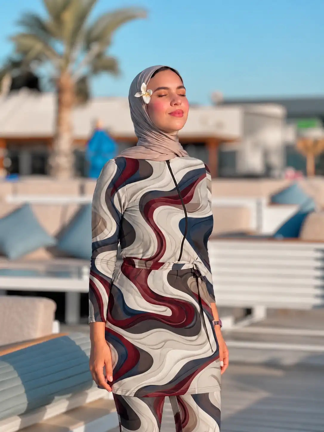Model in a Tallah wave-print burkini with a matching headscarf, with palm trees behind