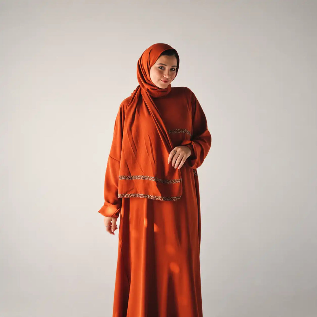 Model in a rust-orange Tallah satin Isdal with a matching headscarf against a plain backdrop