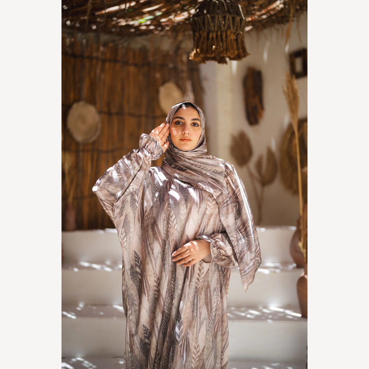 Tallah satin Isdal in beige taupe feather, closer front view with one hand near forehead.
