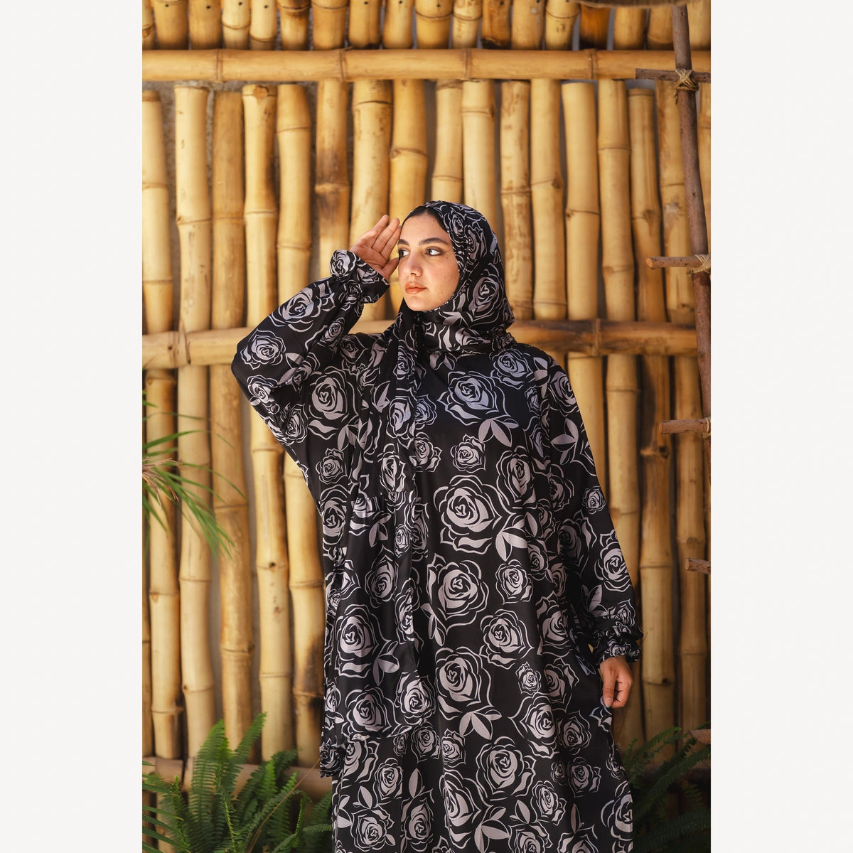 Tallah satin Isdal in black grey rose, closer front view with one hand raised near forehead.