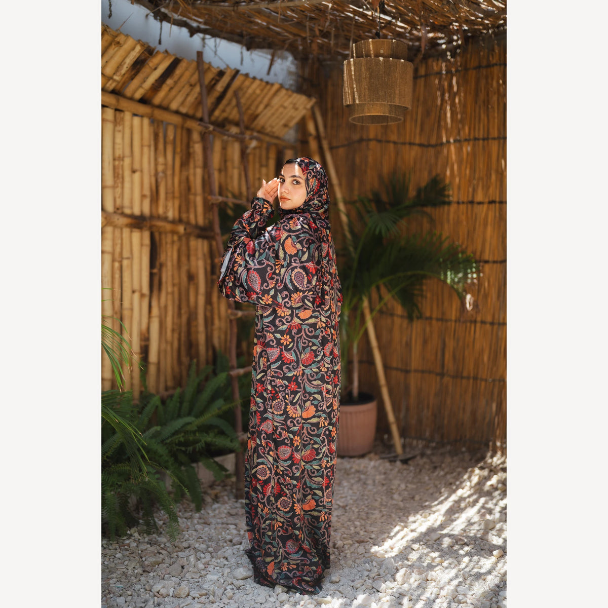Tallah satin Isdal in black red orange paisley, full-length three-quarter view with one hand near face.