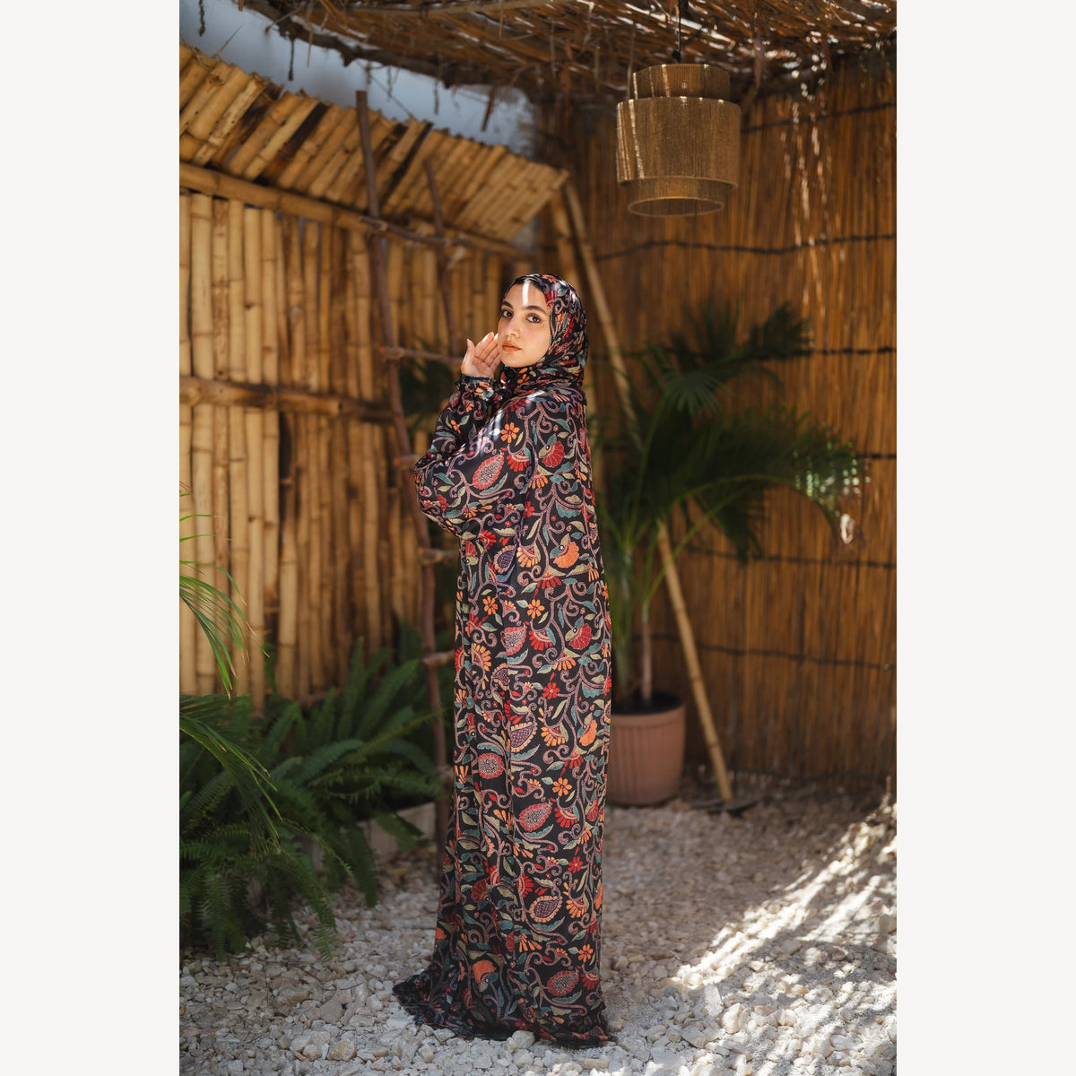 Tallah satin Isdal in black red orange paisley, full-length side view with one hand near face.