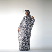 Black and white satin Isdal with paisley and floral motifs, full-length three-quarter view holding the scarf at the shoulder.