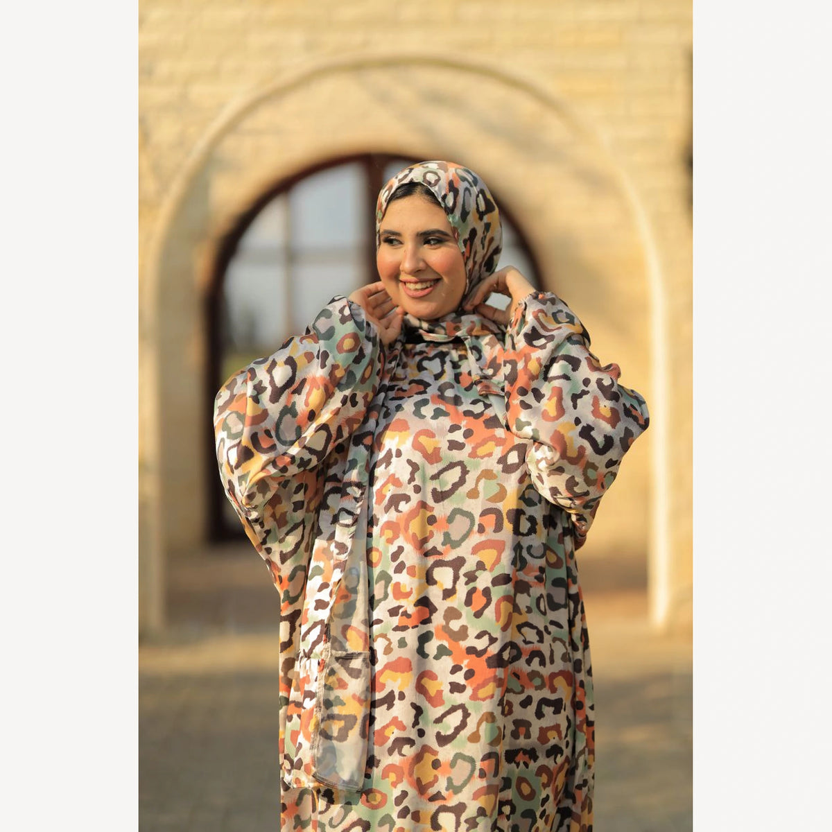 Tallah satin Isdal in cream orange brown leopard, closer front view with hands near head covering.