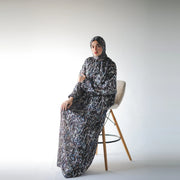 Multicolour satin Isdal with black abstract markings and muted blue and grey accents, full-length seated view on a cream stool.