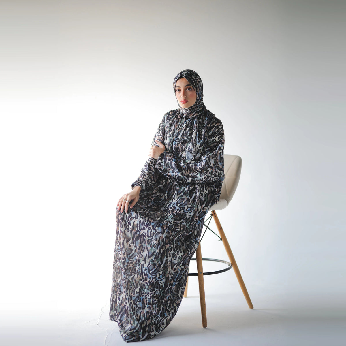 Multicolour satin Isdal with black abstract markings and muted blue and grey accents, full-length seated view on a cream stool.
