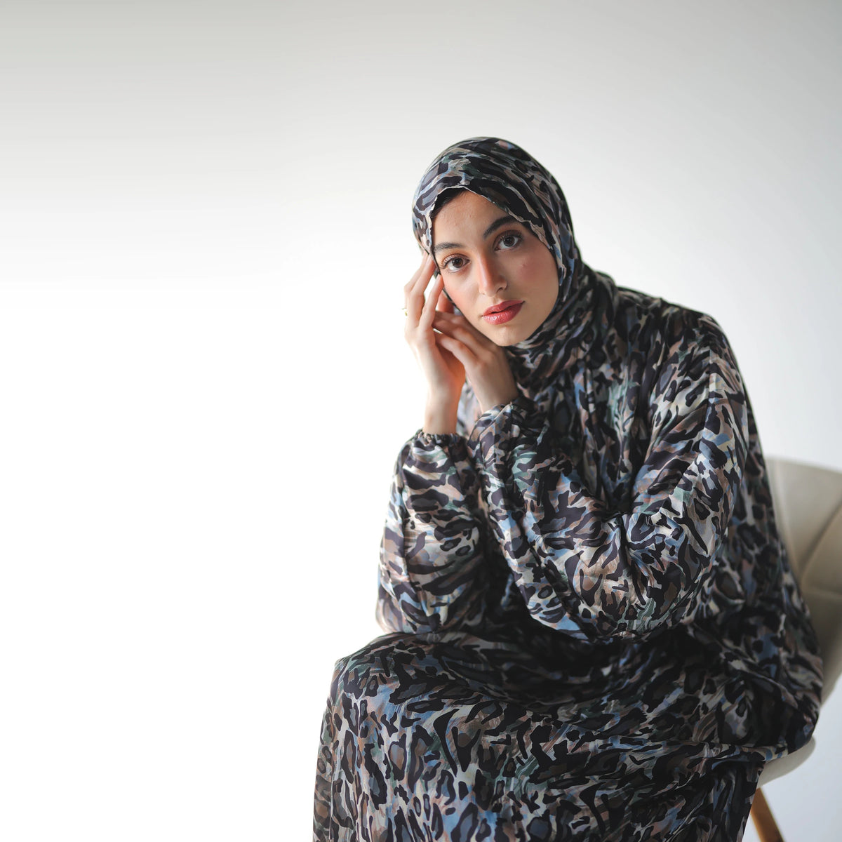 Multicolour satin Isdal with black abstract markings and muted blue and grey accents, seated close-up with hands beside the face.